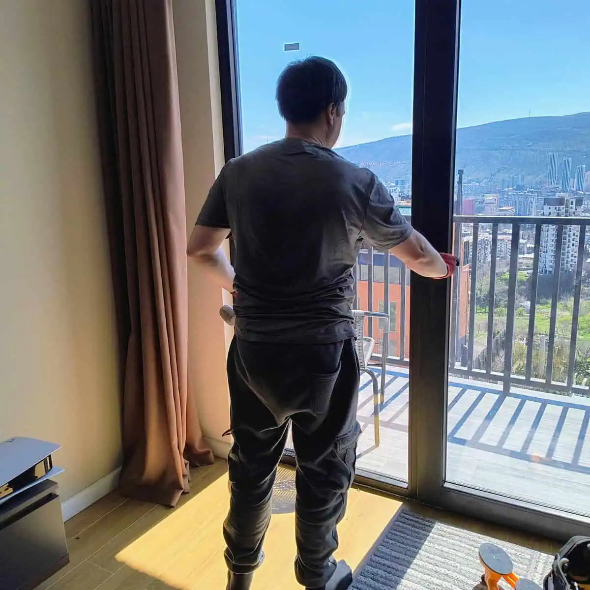 Window fitter adjusting a sliding floor-to-ceiling balcony door in a Tbilisi apartment
