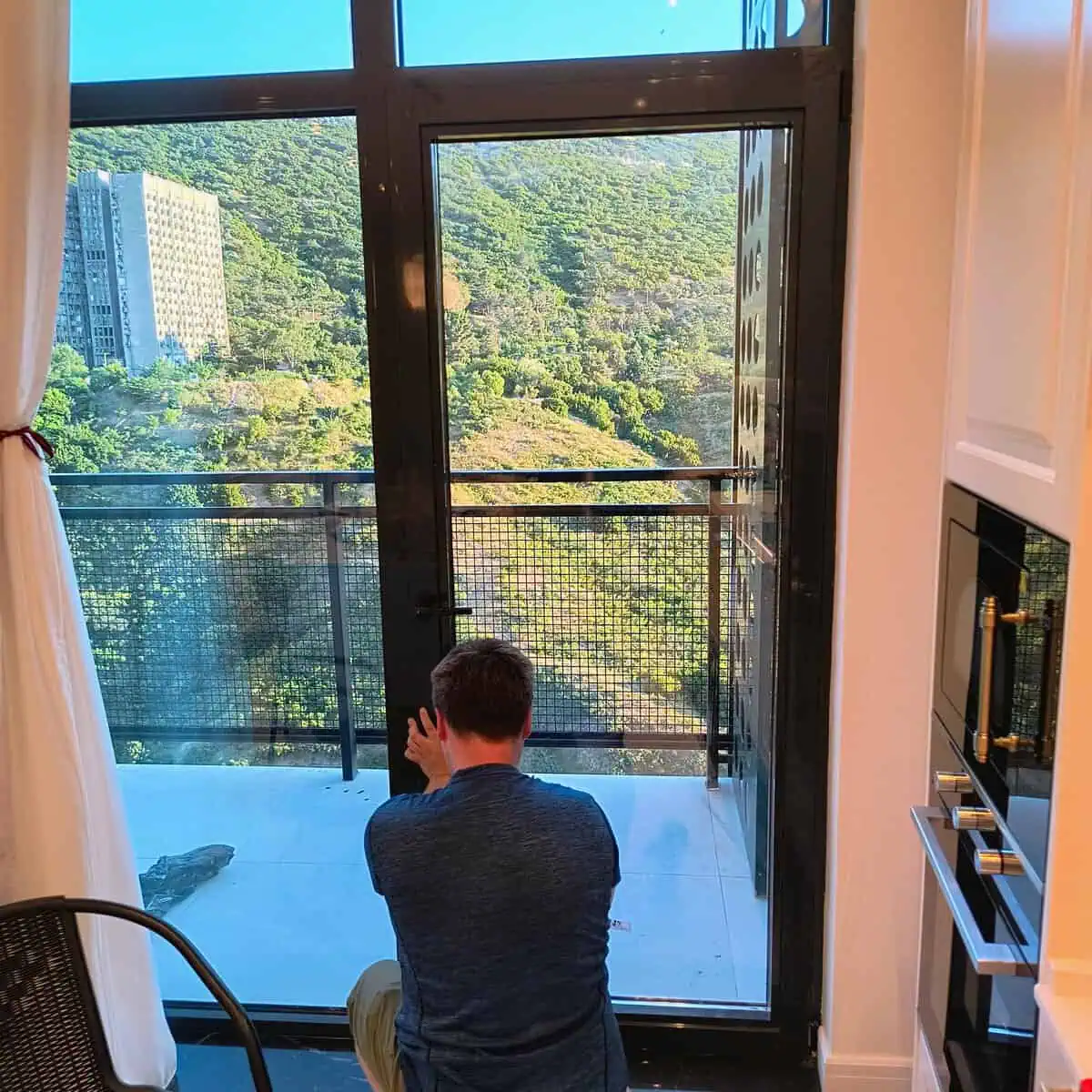 Window fitter securing a new glazing unit in a balcony door overlooking a forested hillside in Tbilisi