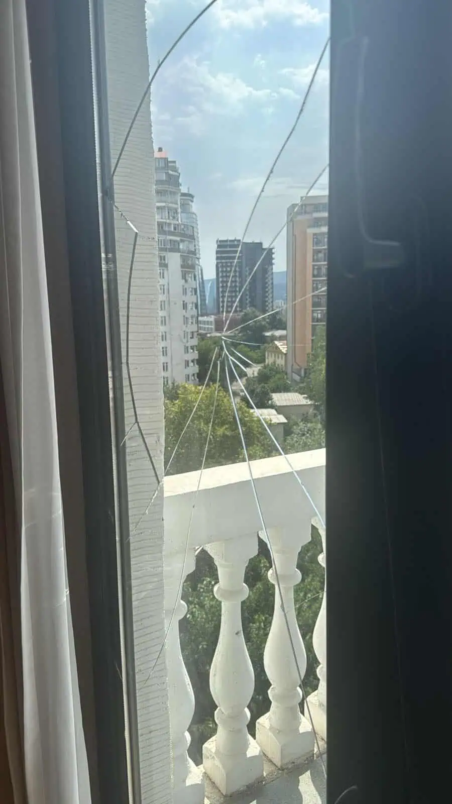 Broken window pane with radiating cracks in a frame overlooking the central district of Tbilisi